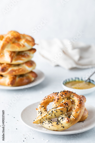 A serving of a baked pretzel served with mustard dip and a stack in behind.
