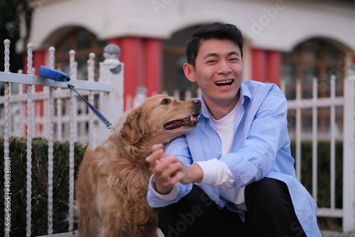 Asian young man and his playful golden retriever pet dog, smiling at camera in public park