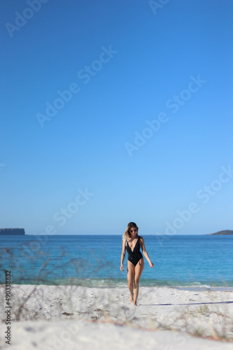 walking young woman in bikini and sunglasses on beach