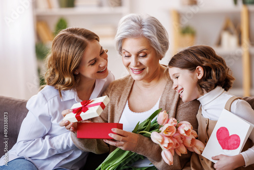 Happy International Women's Day.Smiling  daughter and granddaughter giving flowers  and gift to grandmother   celebrate spring holiday Mother's Day at home © JenkoAtaman