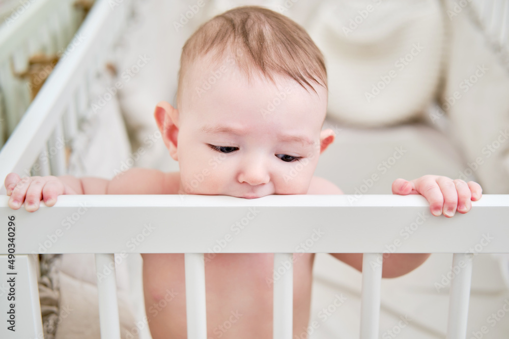 Baby gnaws at the edge crib during teething itching. Funny child scratching his teeth on the rail bed, age six months Baby gnaws at the edge crib during teething itching. Funny child scratching his teeth on the rail bed, age six months