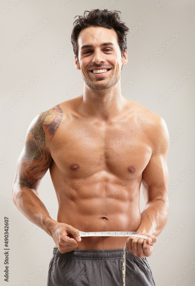 Measuring his perfect abs. Portrait of a hunky young man measuring his waist. Measuring his perfect abs. Portrait of a hunky young man measuring his waist.