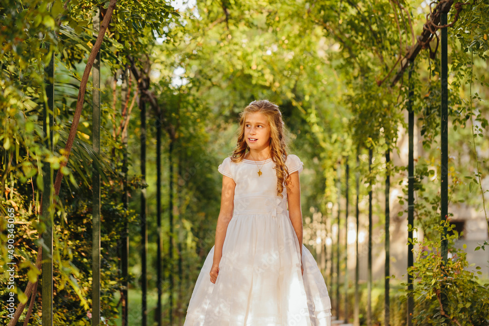Charming girl in First Communion dress standing in park Charming girl in First Communion dress standing in park