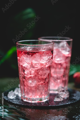 Red drink cocktail or lemonade with ice in a glass on dark background.