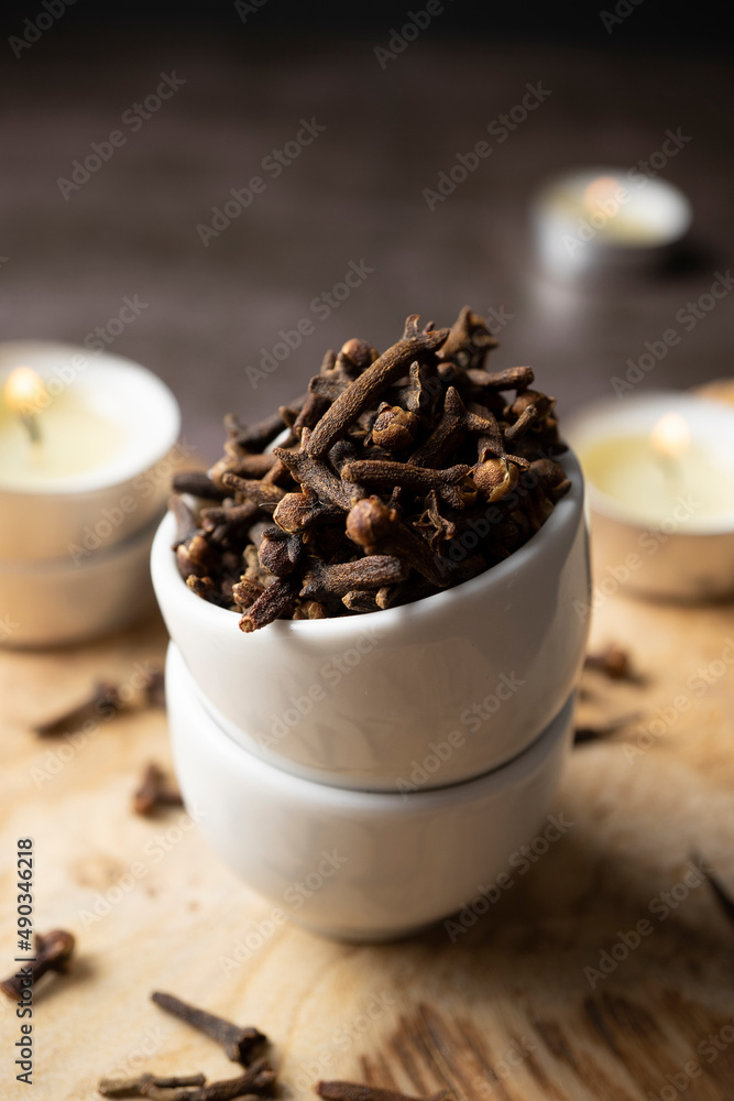 cloves on small white ceramic bowl on wooden board and background with candles cloves on small white ceramic bowl on wooden board and background with candles
