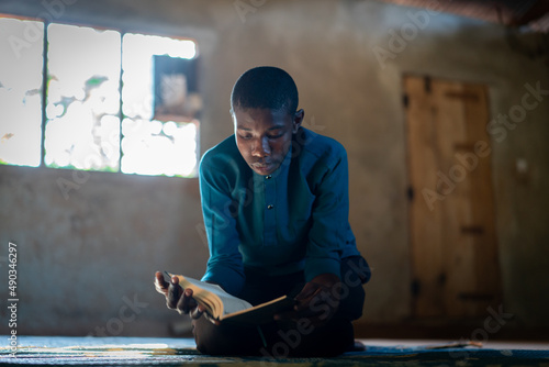 African teenage boy sitting and reading book in poor school, high quality photo
