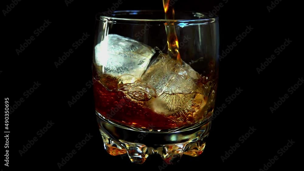 Pouring whiskey into a glass with ice on an isolated black background. Slow motion. Pouring whiskey into a glass with ice on an isolated black background. Slow motion.