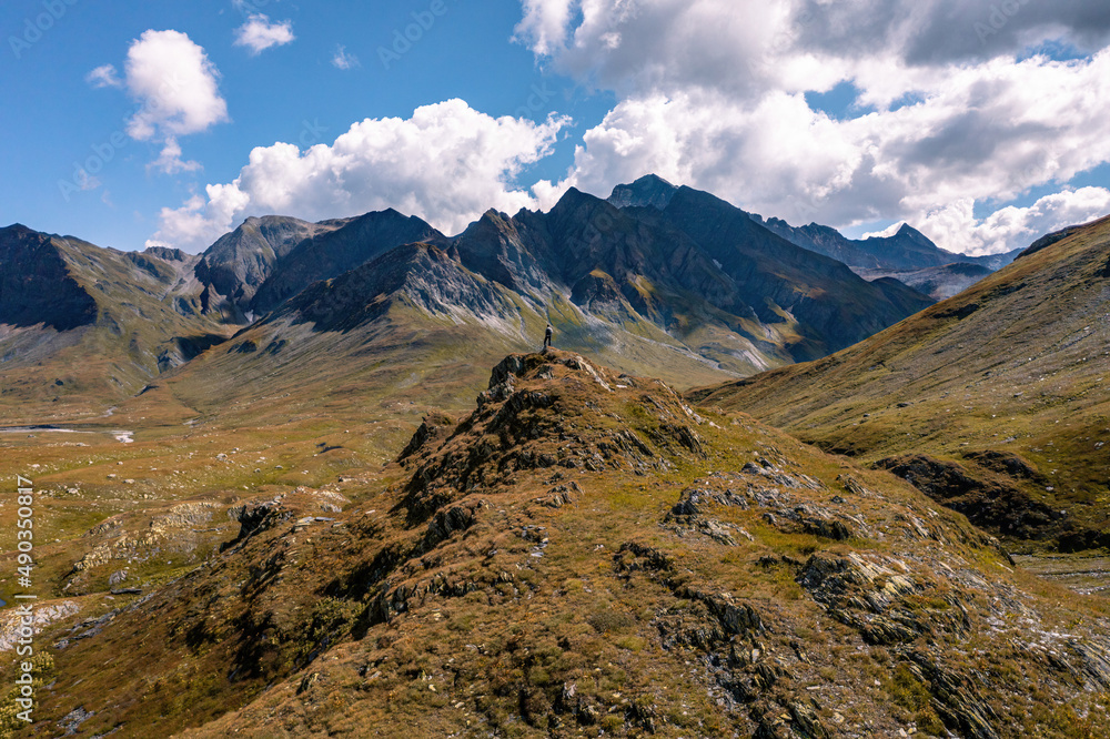 Aerial view toward a man at the tip of a rock formation admiring the vast and majestic alpine landscape, directed toward Piz Ner and Piz Canal, on the Piani della Greina, in Blenio, Switzerland.