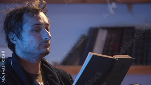 A man in a dressing gown rests in the evening and reads a book at home under a table lamp. Home education and pastime. Close-up