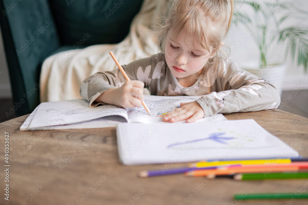 Cute small girl child drawing painting with pencil in album alone, sitting at wooden table. Little kid engaged in art hobby creative activity, spending leisure time at home. Cute small girl child drawing painting with pencil in album alone, sitting at wooden table. Little kid engaged in art hobby creative activity, spending leisure time at home.