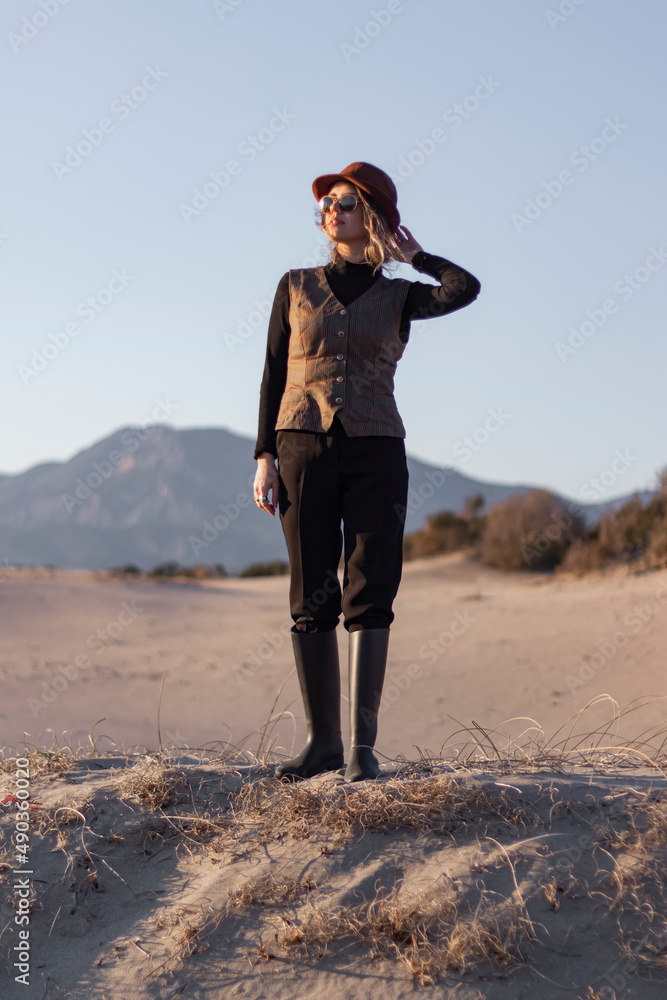 Stylish young woman spending time outdoor. Fresh air concept. Graceful young lady in brown clothes, sun glasses and hat enjoying views.	