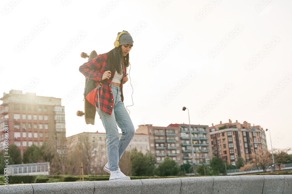 Obraz premium young latina walking in the city with a backpack and a skateboard. Venezuelan Hispanic woman practicing sport.