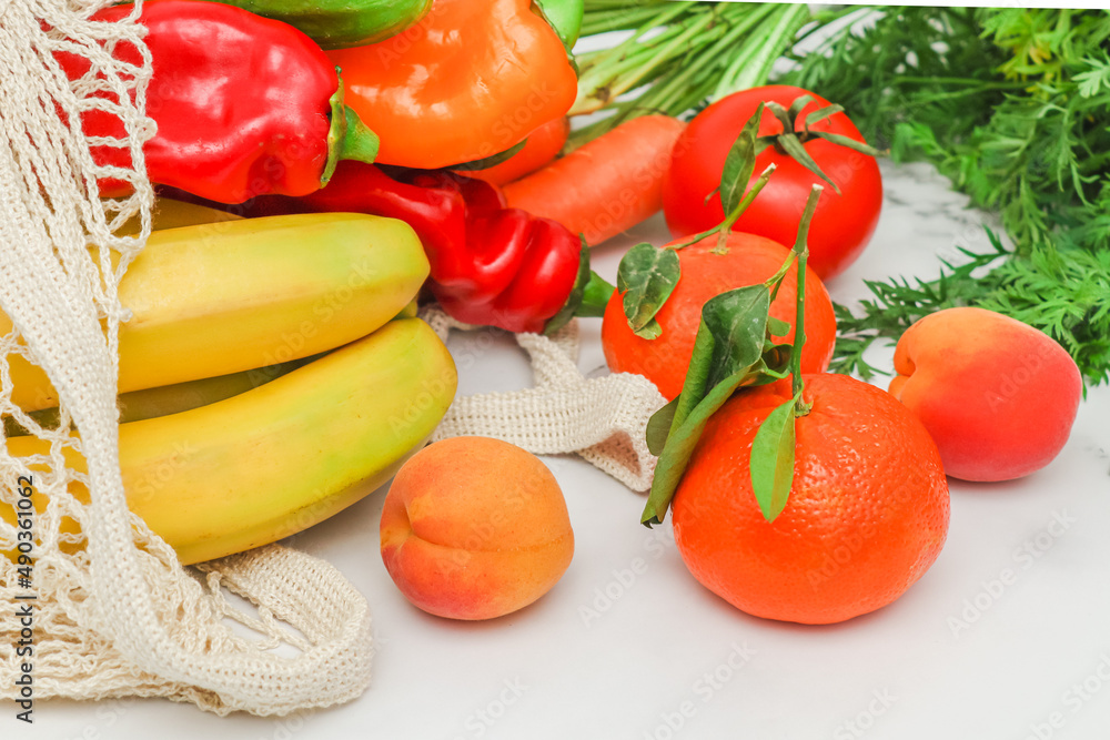 Seasonal vegetables and fruits: bananas, peppers, tangerines, apricots and tomatoes in a cotton mesh.