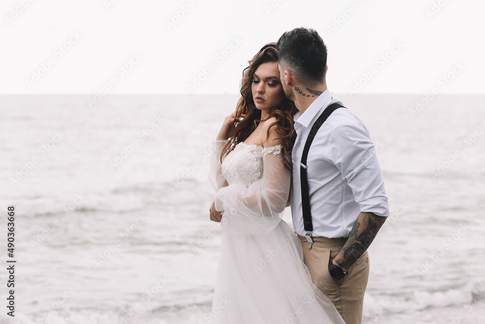The bride and groom in wedding dresses hug and walk together along the sea in nature on an outdoor trip. Husband and wife in love spend their honeymoon. Selective focus
