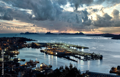 Vista general y panorámica de Vigo ciudad y su puerto al anochecer con las Islas Cíes en el horizontes un cielo con nubes muy dramático  