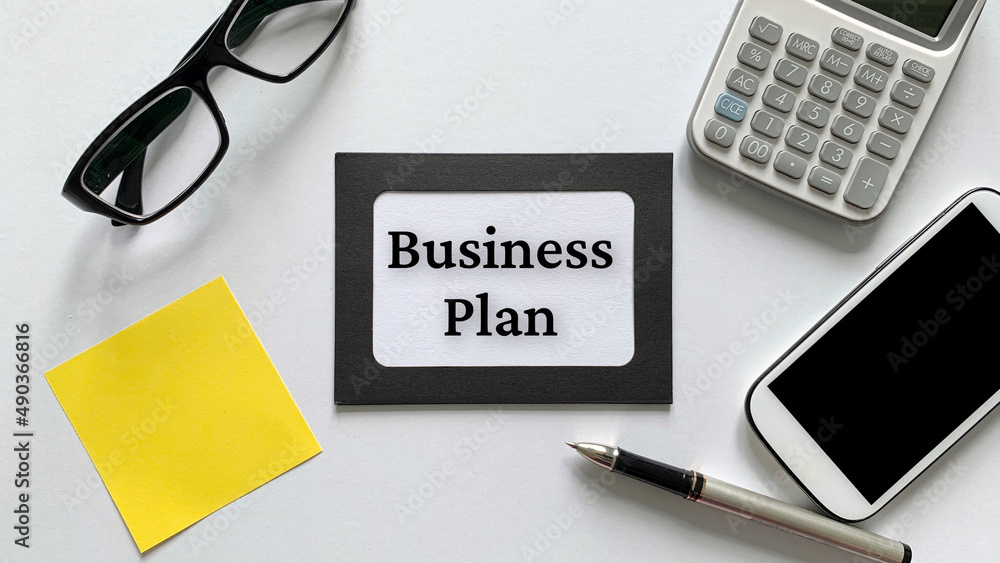 Business plan text on notepad with glasses, calculator, phone and yellow sticky note background. Business concept. Business plan text on notepad with glasses, calculator, phone and yellow sticky note background. Business concept.