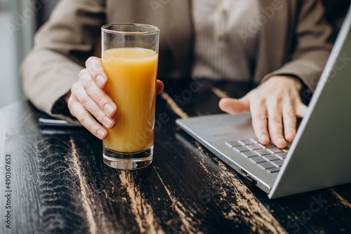 Woman drinking juice and using laptop in a cafe close up