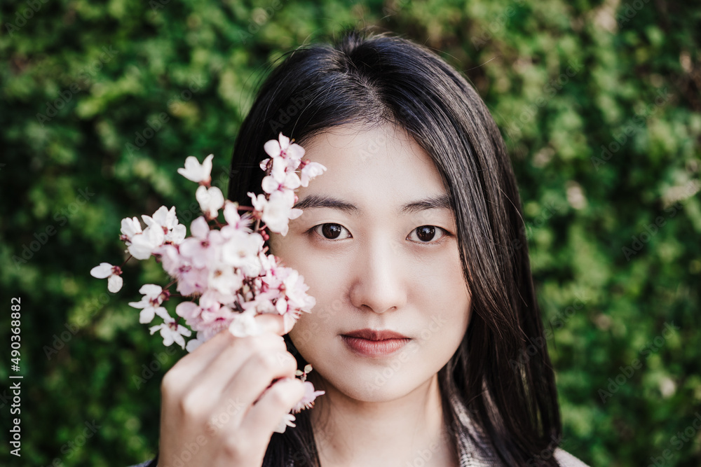 portrait of beautiful chinese asian woman holding almond tree flowers. Springtime outdoors