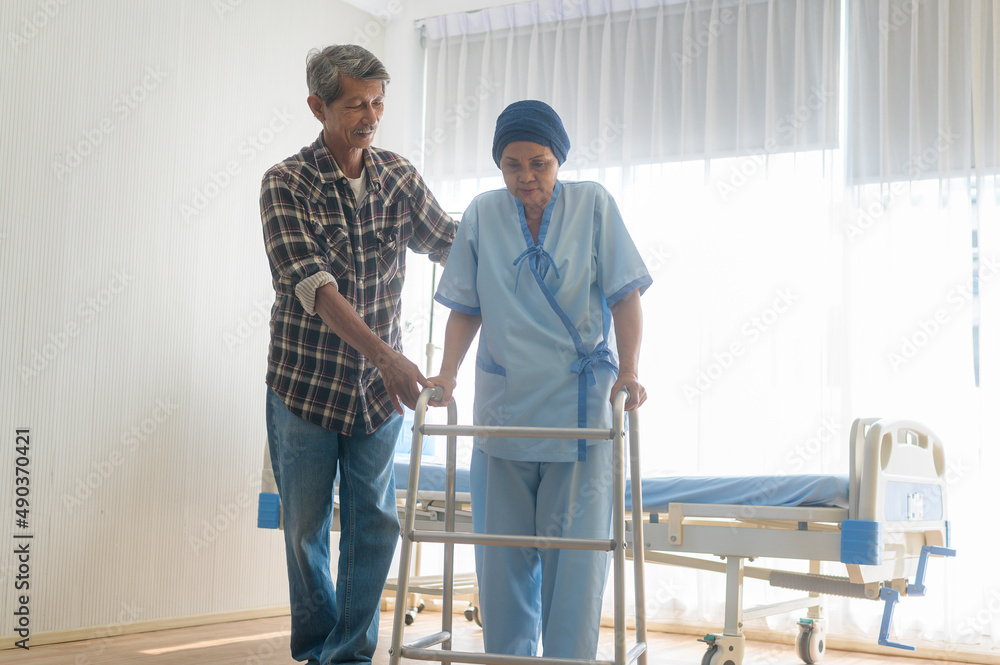 Senior man helping cancer patient woman wearing head scarf with walker at hospital, health care and medical concept
