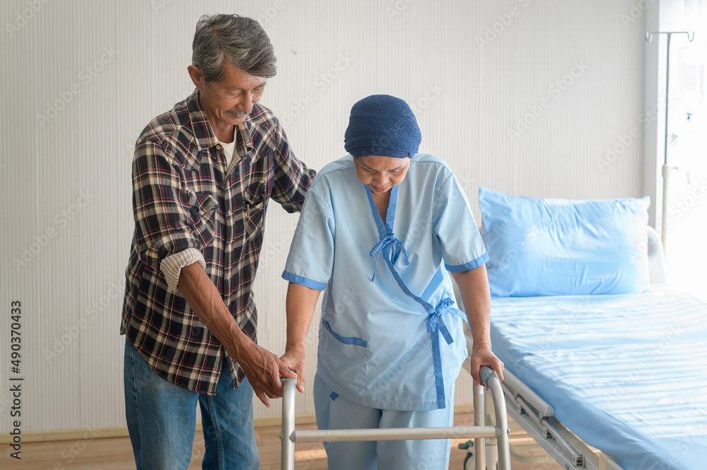 Senior man helping cancer patient woman wearing head scarf with walker at hospital, health care and medical concept