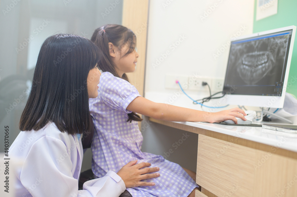 Female dentist explaining teeth x-ray to a little girl in dental clinic, teeth check-up and Healthy teeth concept Female dentist explaining teeth x-ray to a little girl in dental clinic, teeth check-up and Healthy teeth concept