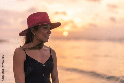 Young latin girl wearing a red hat on the beach at sunset