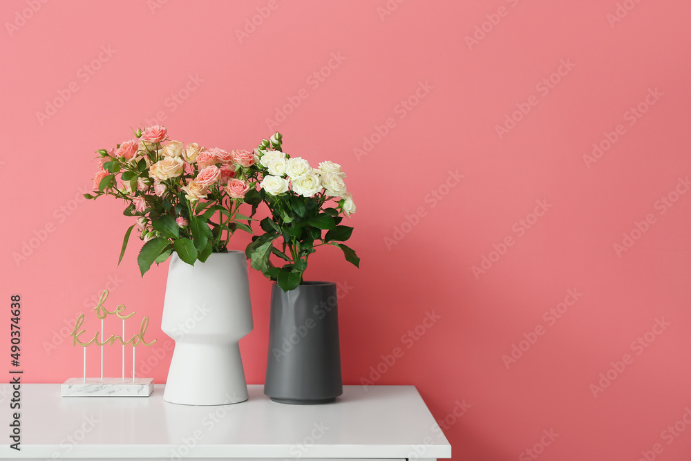 Vases with beautiful roses and decor on table near pink wall