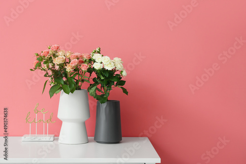 Vases with beautiful roses and decor on table near pink wall
