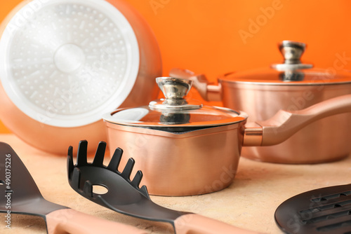 Copper kitchen utensils on table against orange background, closeup
