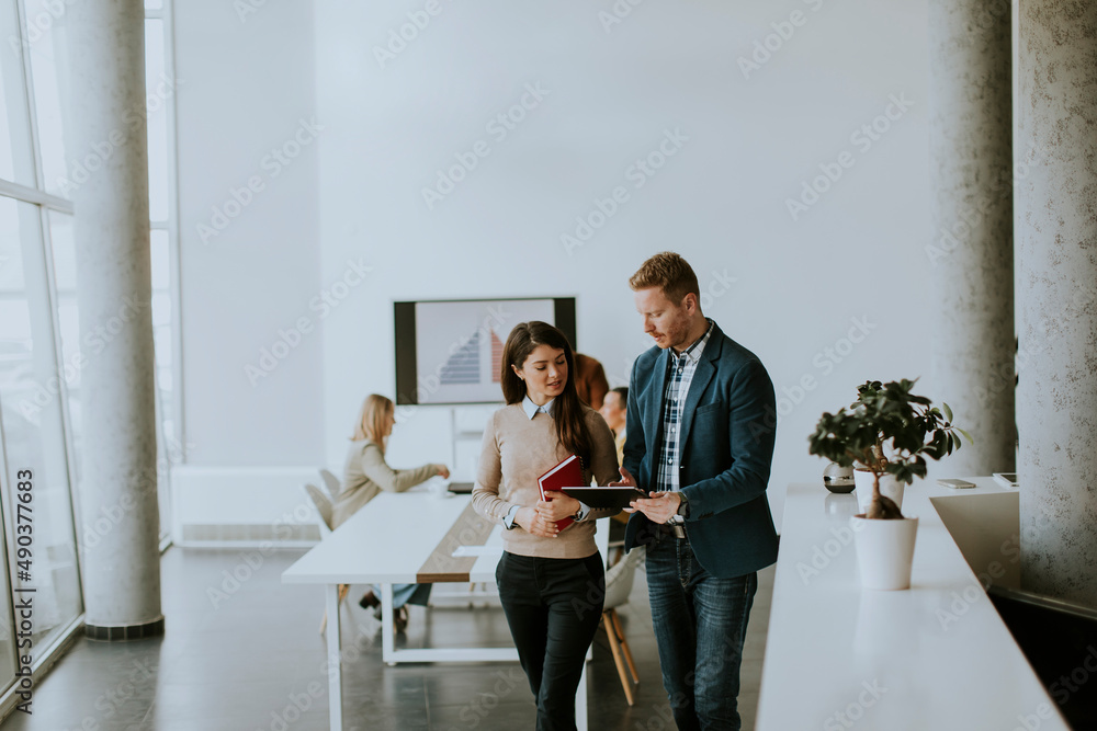 Young entrepreneur couple walking together and using digital tablet in the modern office