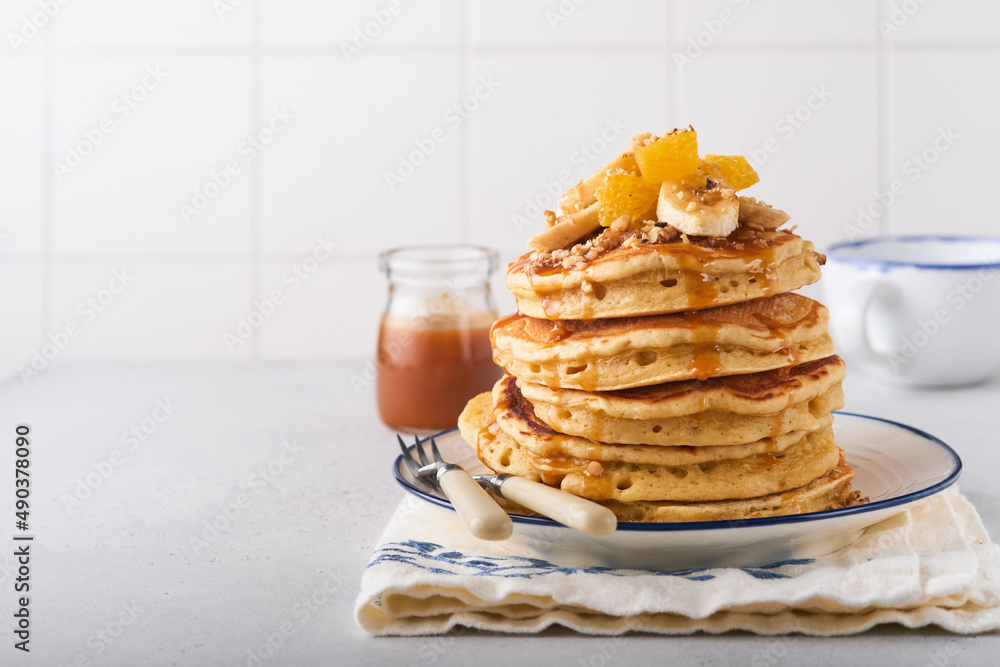 Pancakes. Homemade fluffy pancake with banana, walnut and caramel for breakfast on light concrete background. Delicious pancakes for traditional American breakfast. Selective focus. Mock up. Pancakes. Homemade fluffy pancake with banana, walnut and caramel for breakfast on light concrete background. Delicious pancakes for traditional American breakfast. Selective focus. Mock up.