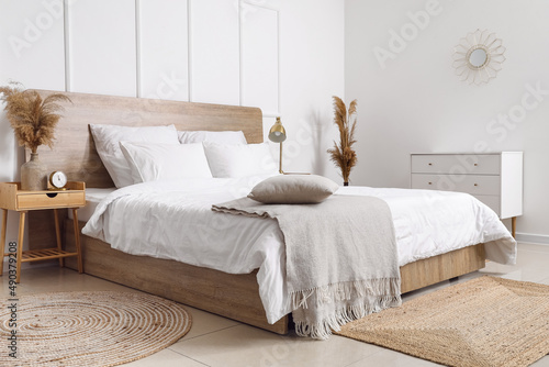 Comfortable bed, dry reeds and chest of drawers near white wall photo