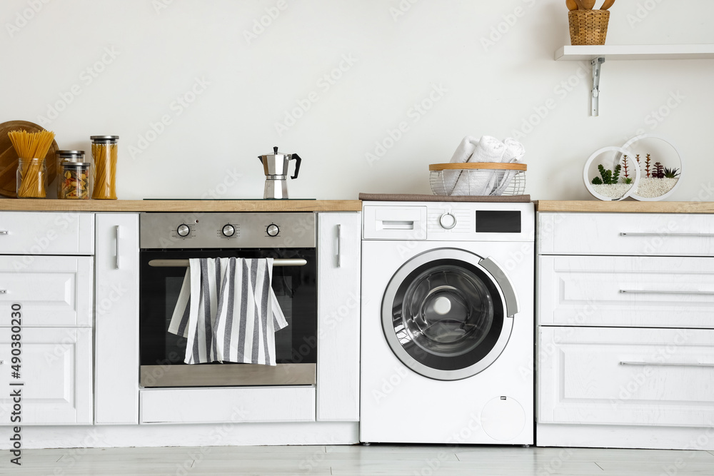Interior of light kitchen with washing machine, oven and white counters Interior of light kitchen with washing machine, oven and white counters