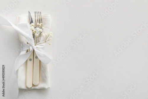 Elegant cutlery and flowers on light background