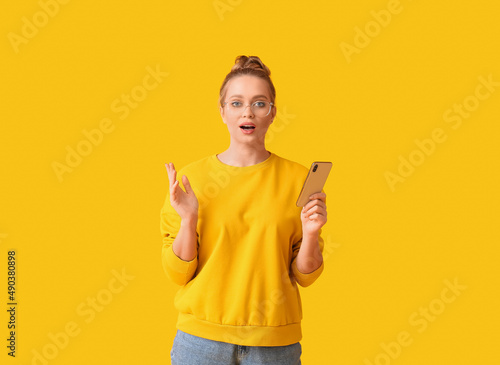 Surprised young woman with mobile phone on yellow background
