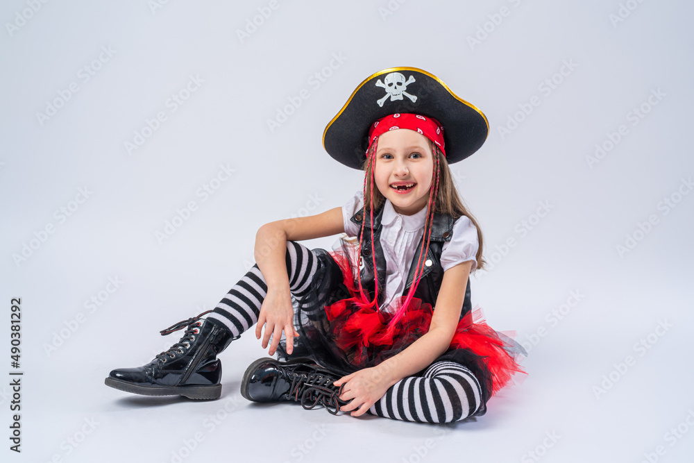 Obraz premium Portrait of a naughty little girl in a pirate costume, sitting on a whrite background, A girl is preparing for the Halloween holiday.