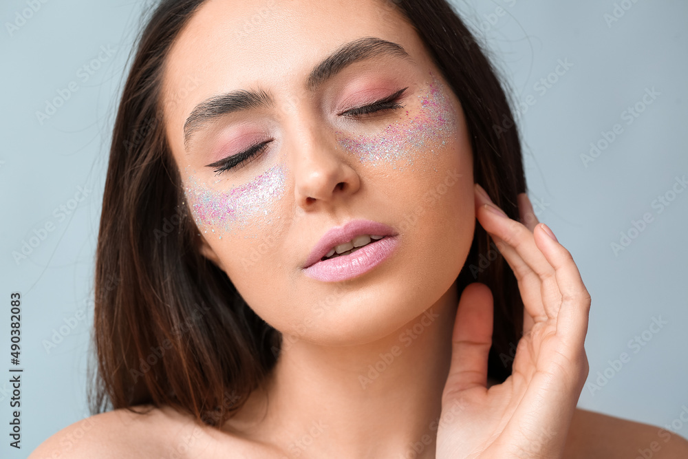 Beautiful young woman with glitters on her face against light background Beautiful young woman with glitters on her face against light background