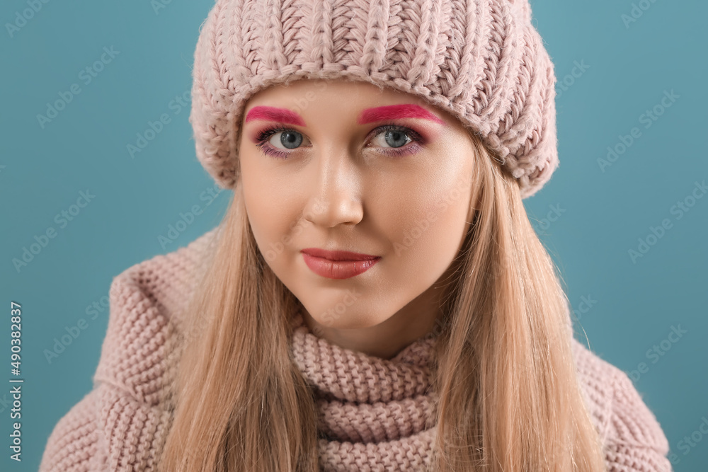 Portrait of woman with creative eyebrows in knitted hat on color background