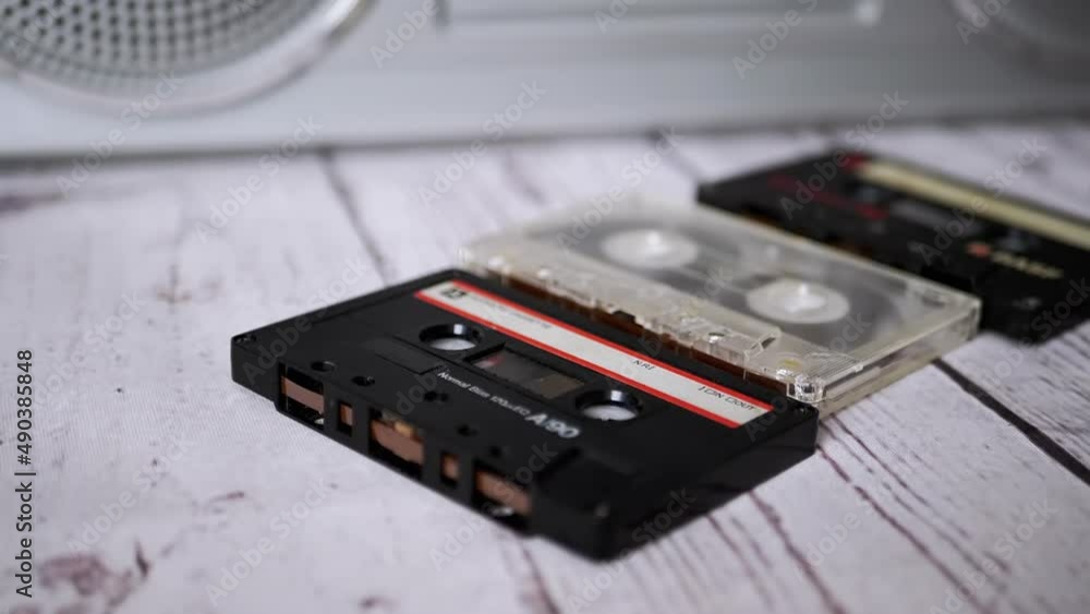 Lots of Falling Audio Cassettes on Table Domino Effect. A pile, a stack of vintage, obsolete, magnetic tape cassettes from the late 80s, 90s lie on a table near of a tape recorder. Nostalgia. Music. Lots of Falling Audio Cassettes on Table Domino Effect. A pile, a stack of vintage, obsolete, magnetic tape cassettes from the late 80s, 90s lie on a table near of a tape recorder. Nostalgia. Music.
