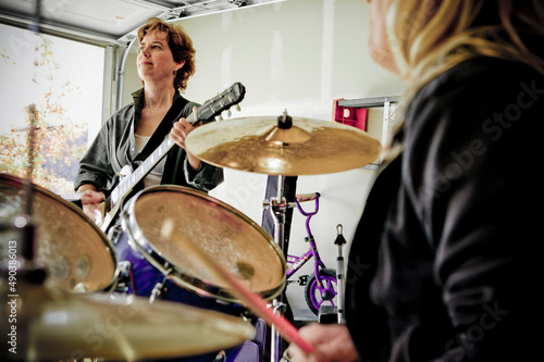 View over drummers shoulder of guitar player in Garage band composed of middle aged women, practicing in residential garage  photo