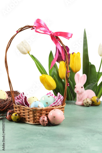Basket with painted Easter eggs and tulip flowers on table against white background
