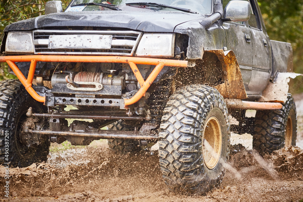 Traveling off-road on dirty off-road on a black and orange truck. Close-up of the wheel, suspension in a puddle and mud Traveling off-road on dirty off-road on a black and orange truck. Close-up of the wheel, suspension in a puddle and mud