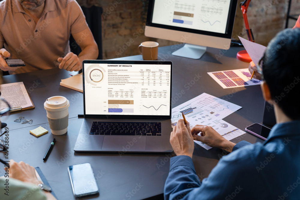 Close-up of business people sitting at the table with laptop and looking at monitor with financial grpahs during teamwork at meeting Close-up of business people sitting at the table with laptop and looking at monitor with financial grpahs during teamwork at meeting