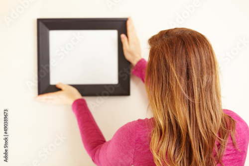 Picture perfect. Rearview shot of a woman placing an empty frame on a wall.