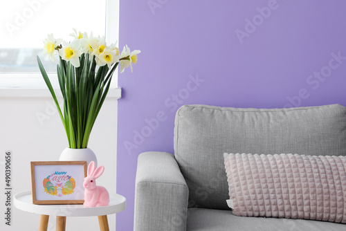 Vase with flowers  Easter rabbit and greeting card on table near sofa