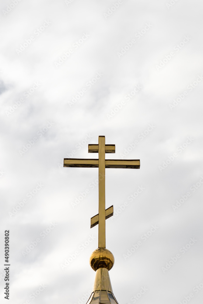 Orthodox cross on the background of a cloudy sky. Vertical photograph of the church cross.