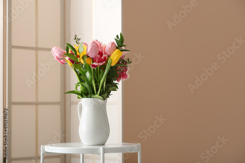 Vase with spring flowers on table and folding screen near beige wall