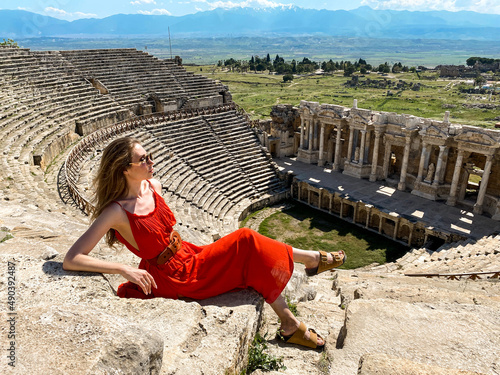 A young beautiful woman in a red dress walking in Pamukkale, Turkey, against the backdrop of the ruins of the ancient city of Hierapolis