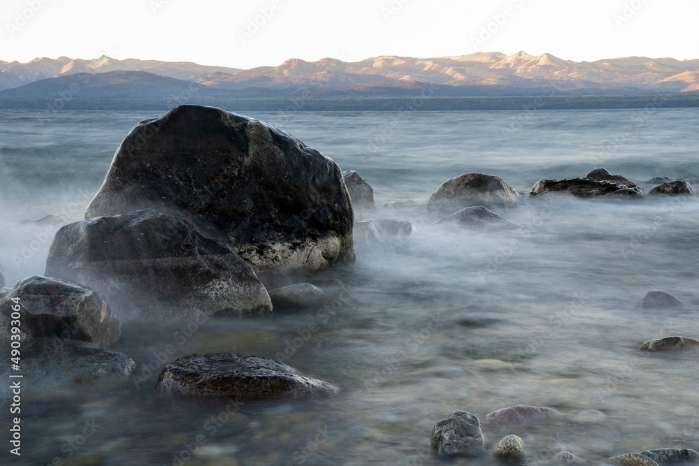Naklejka premium Long exposure shot of Nahuel Huapi lake at sunset. Beautiful blurred water effect, the rocky shore and dusk colors.
