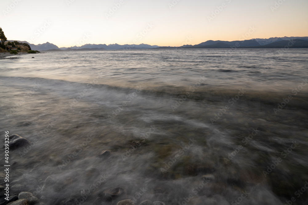 Fototapeta premium Long exposure shot of Nahuel Huapi lake at sunset. Beautiful blurred water effect, the rocky shore, waves and dusk colors .